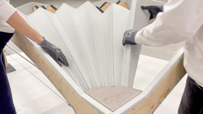 Unfold Form consists of a plywood sheet cut into individual curved strips with textile layers applied to one side to connect them. The plywood strips can be unfolded like a fan on site, causing them to bend into shape.